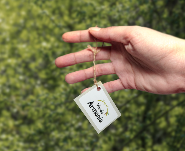 Persona mostrando en primer plano la etiqueta para Verde Armonía con un fondo de arbustos